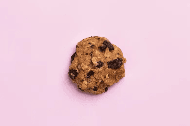 A single chocolate chip cookie on a pink background.