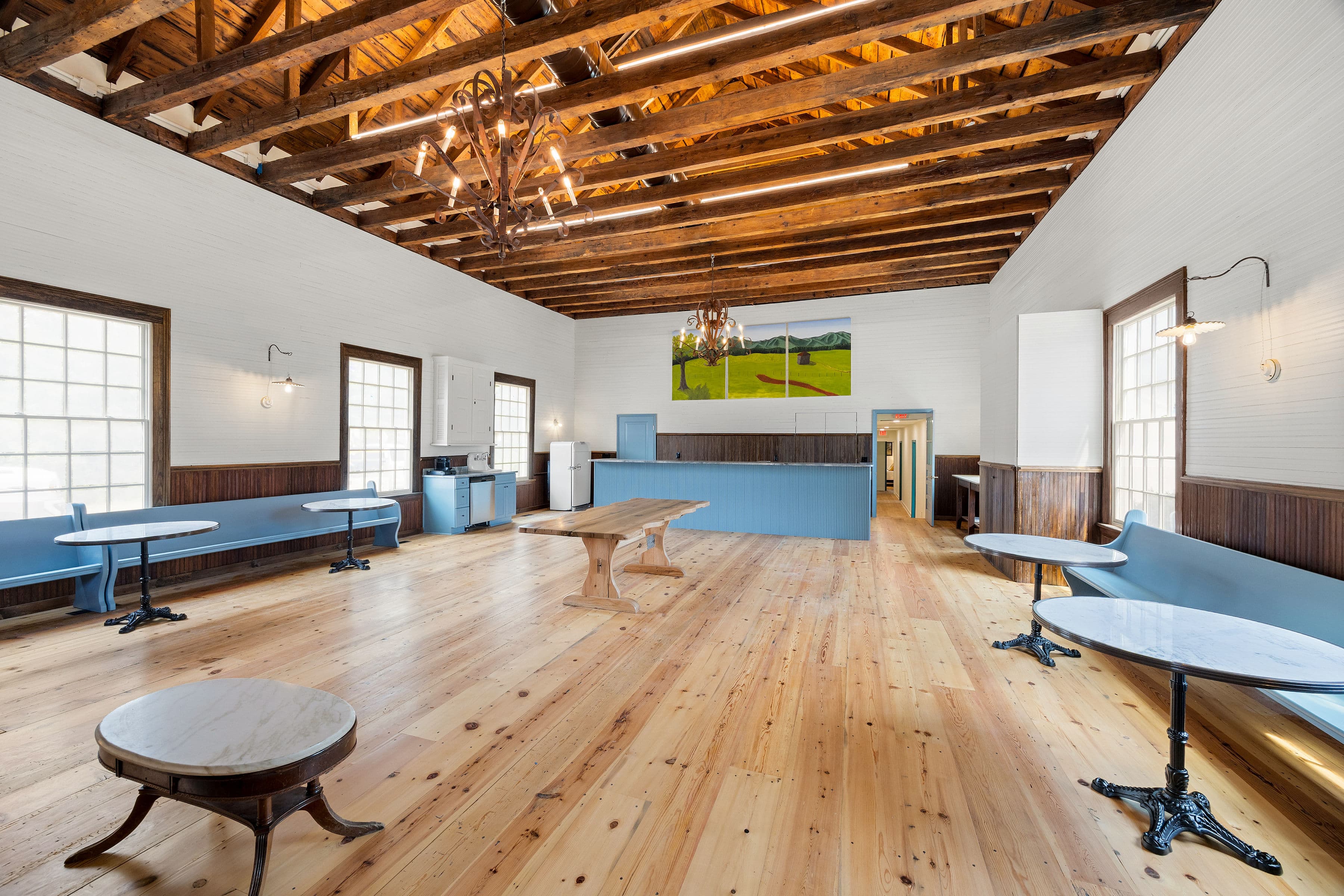 A spacious, well-lit interior room with wooden floors, high ceilings, and blue benches along the walls.