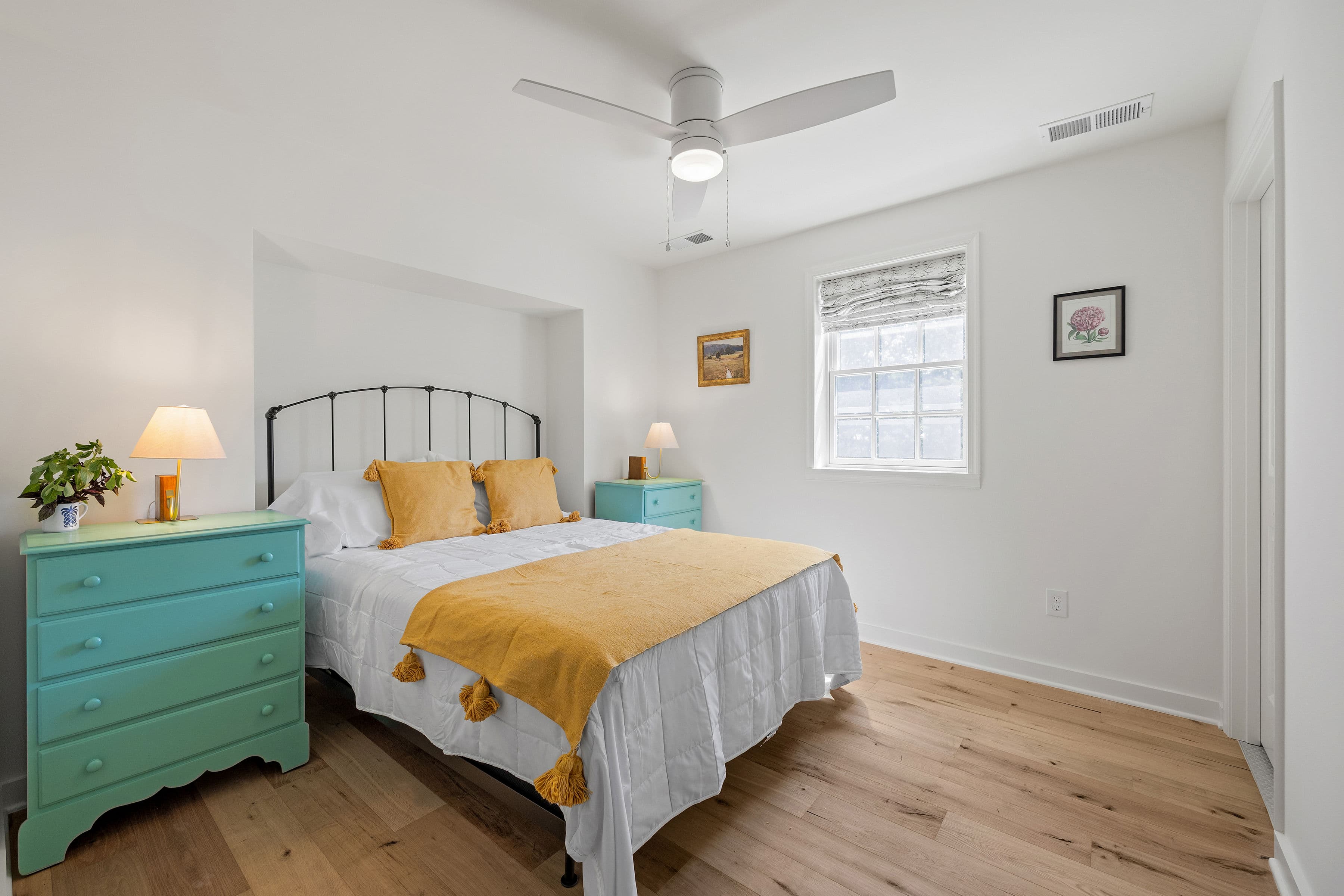 Bright and modern bedroom featuring a bed with yellow accents, turquoise nightstands, and a ceiling fan.
