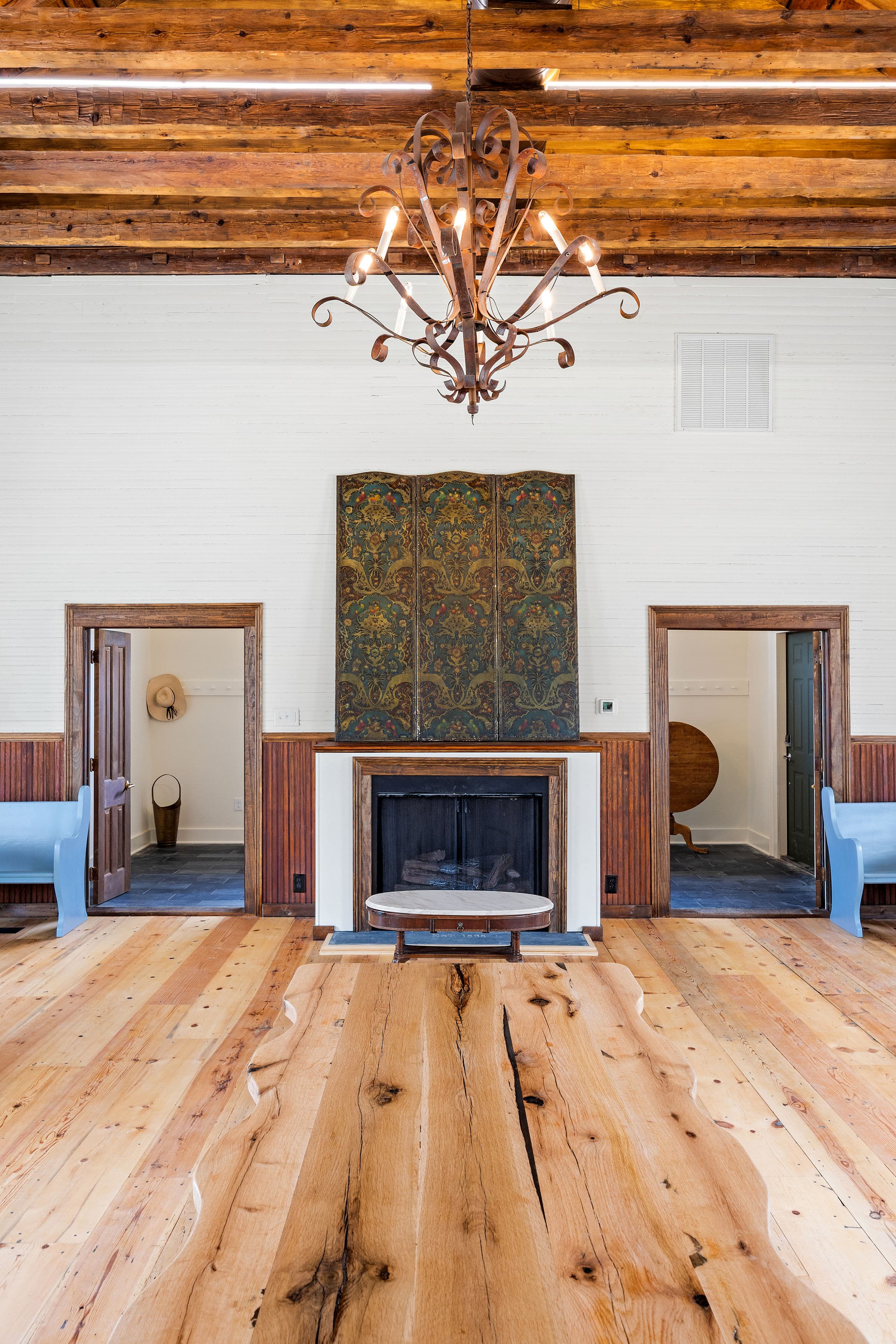 A spacious room featuring wooden beams, a chandelier, and a decorative fireplace with two doorways on either side.