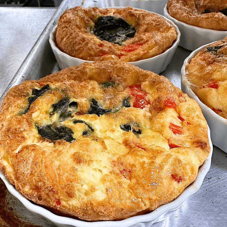 A close-up of freshly baked savory soufflés with spinach and tomatoes in white ramekins.