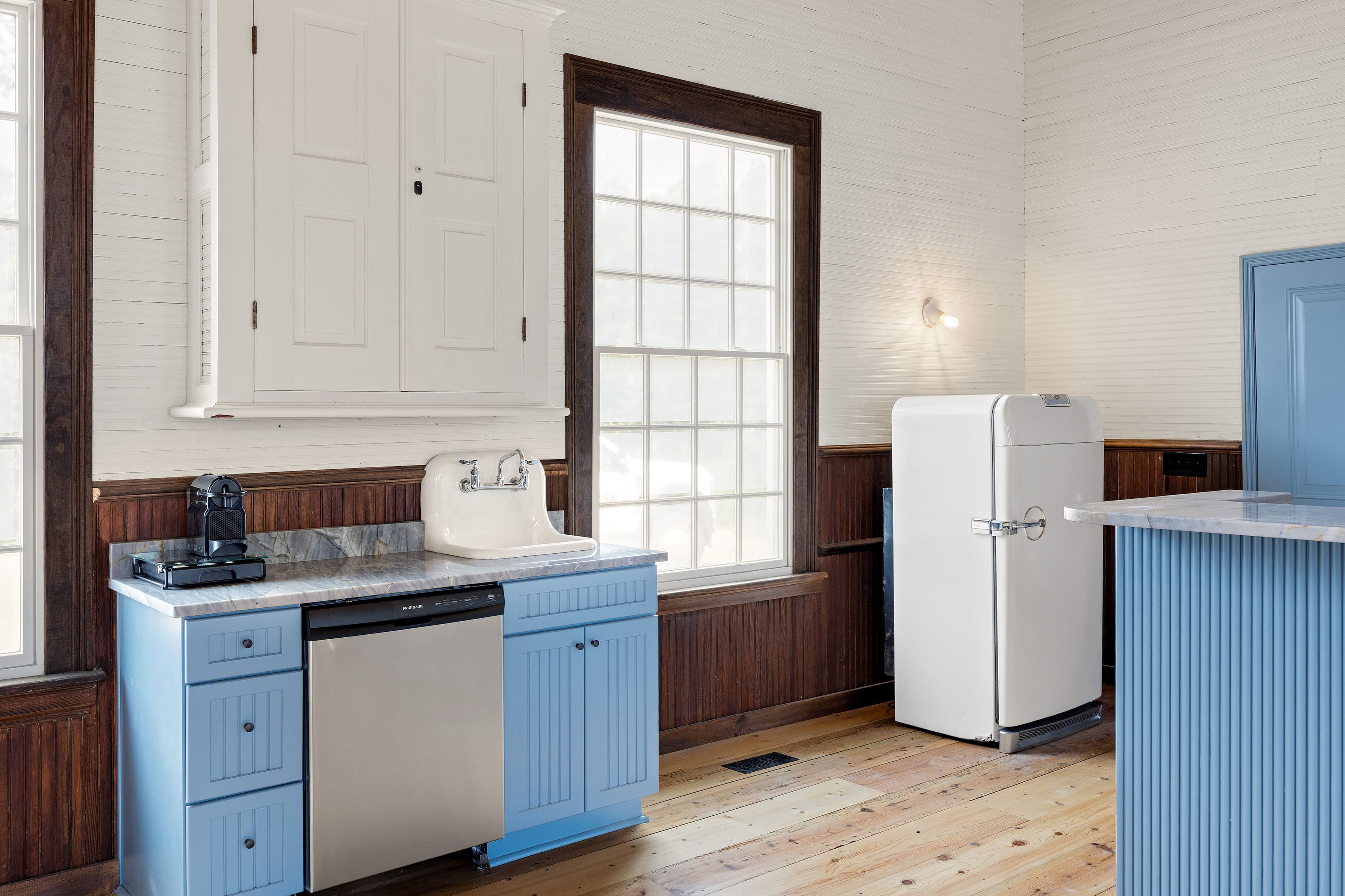 A modern kitchen with blue cabinets, stainless steel appliances, and large windows letting in natural light.