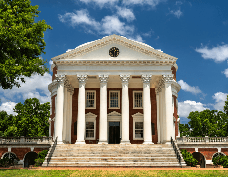 The front of a classical building featuring large white columns and a clock under a blue sky.