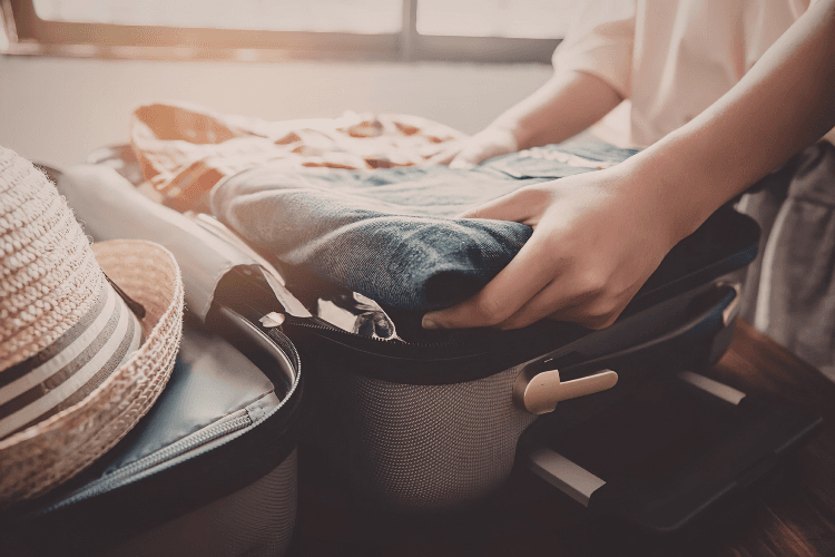 A person packs a suitcase with clothing and a hat.