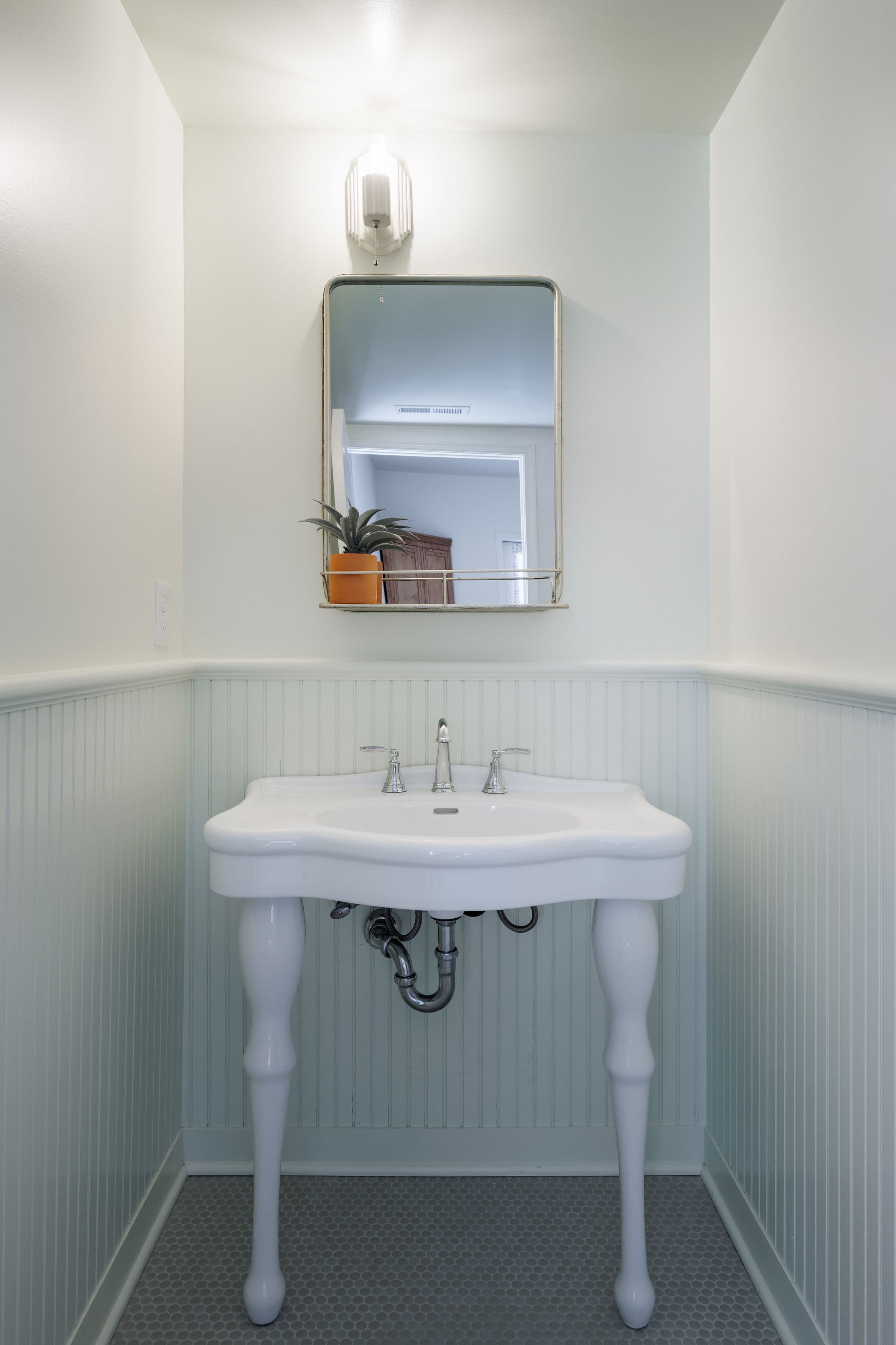 A small bathroom featuring a white pedestal sink, a mirror, and a wall-mounted light, with green wainscoting.