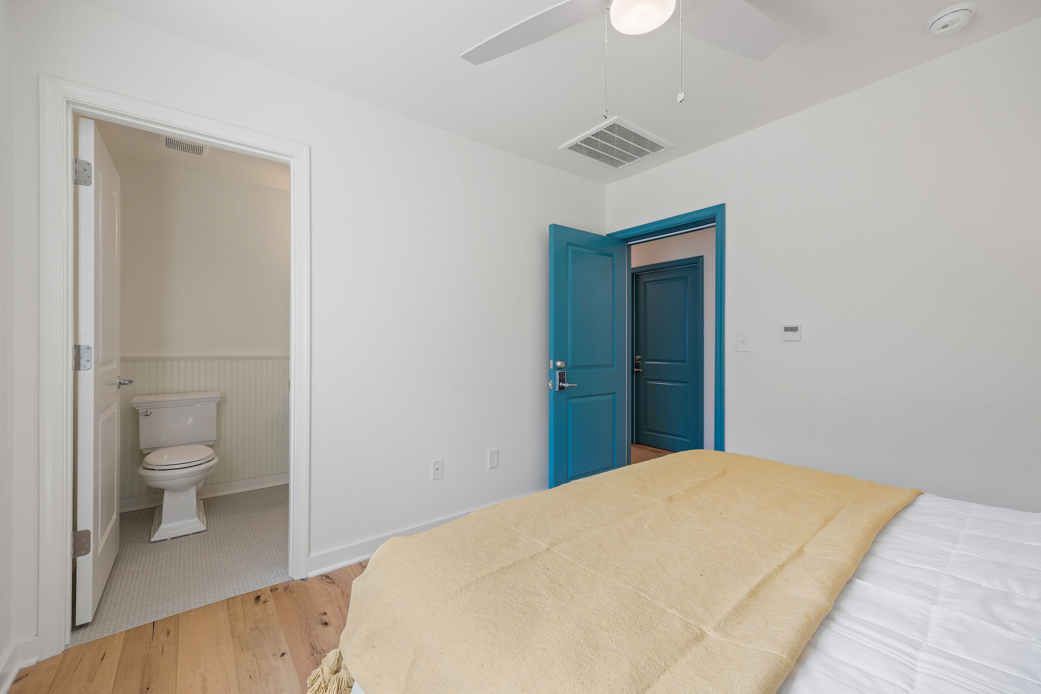 A cozy bedroom with a bed topped with a yellow blanket and an open door leading to a bathroom.