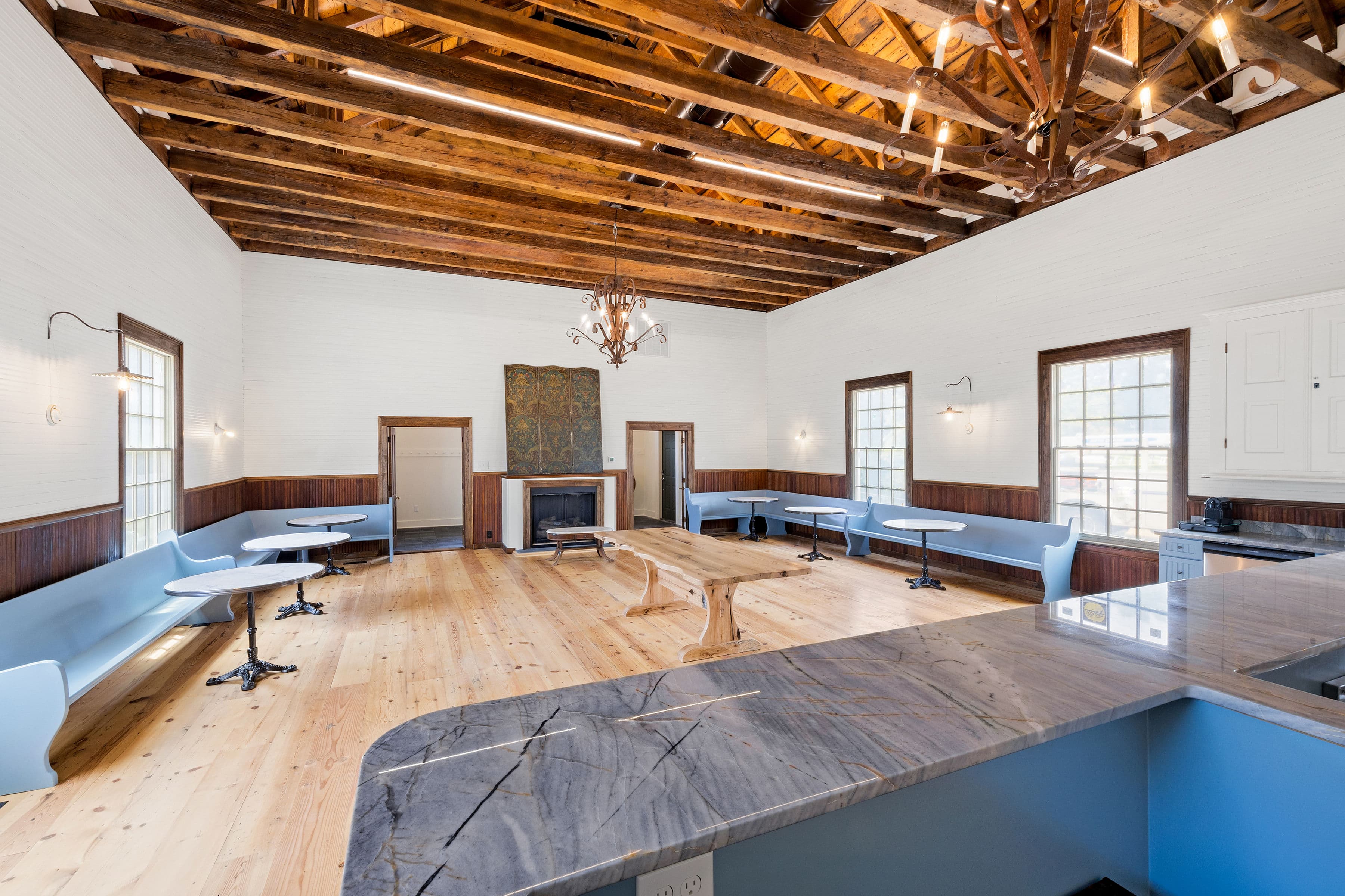 A spacious, well-lit room with wooden beams, featuring blue seating and a central table.