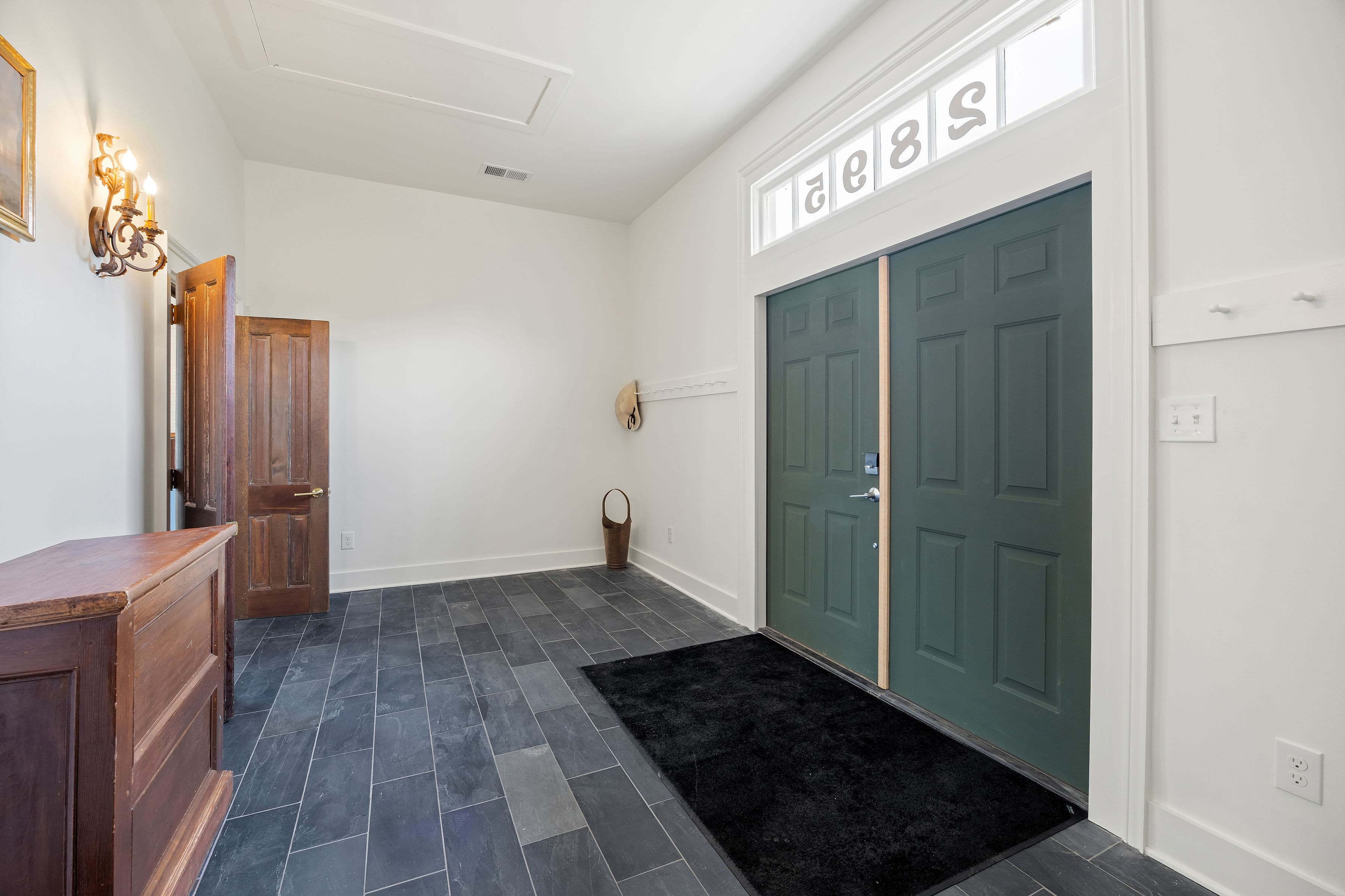 A spacious entryway featuring green double doors, dark tile flooring, and a small table with a mirror.
