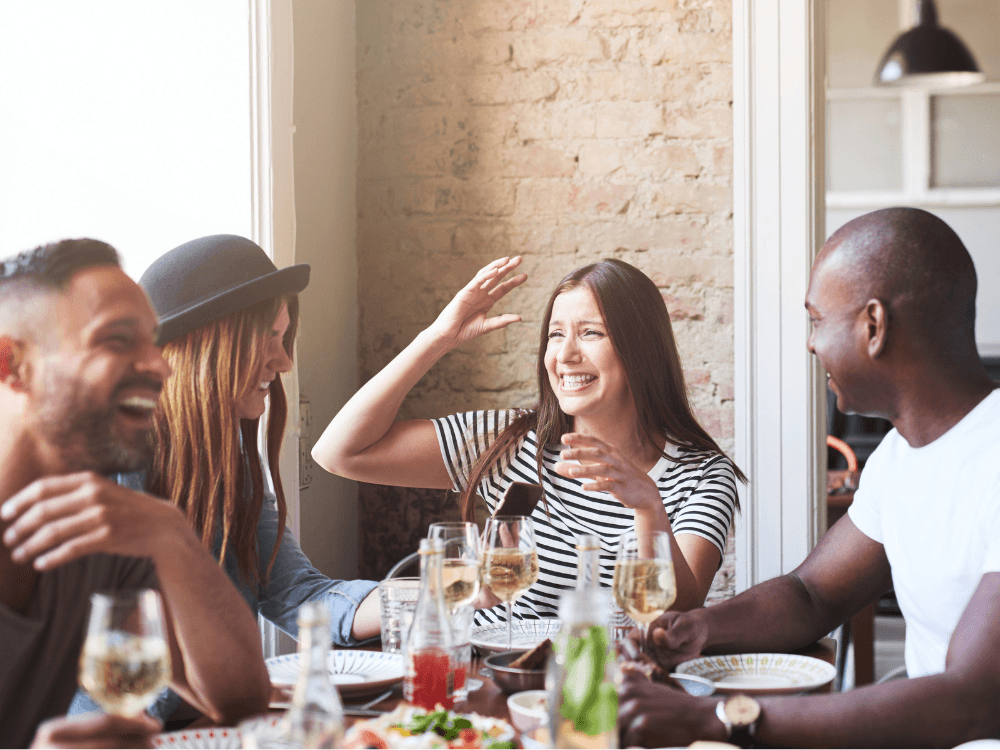 A group of four friends enjoy a lively conversation over drinks and food at a table.