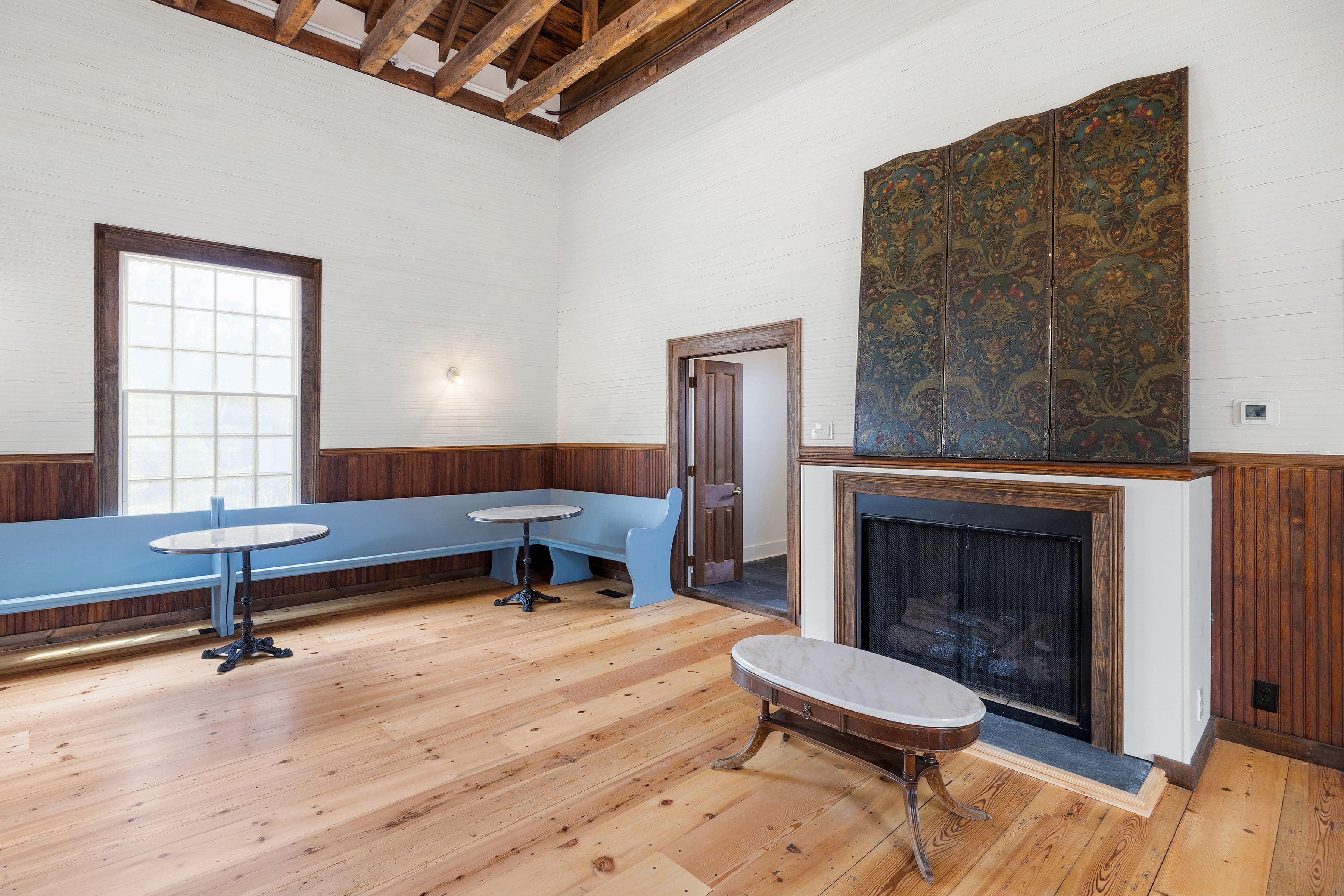 A spacious room with wooden floors, blue seating, small tables, and a decorative fireplace.