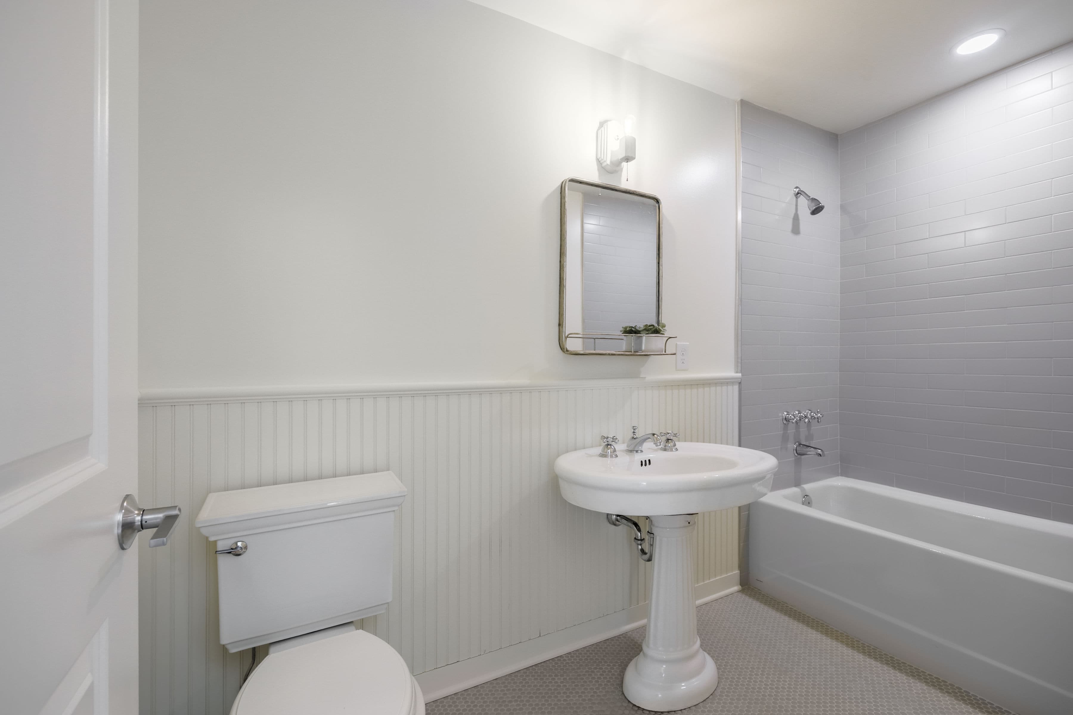 A clean, modern bathroom featuring a sink, toilet, mirror, and a bathtub with a showerhead.