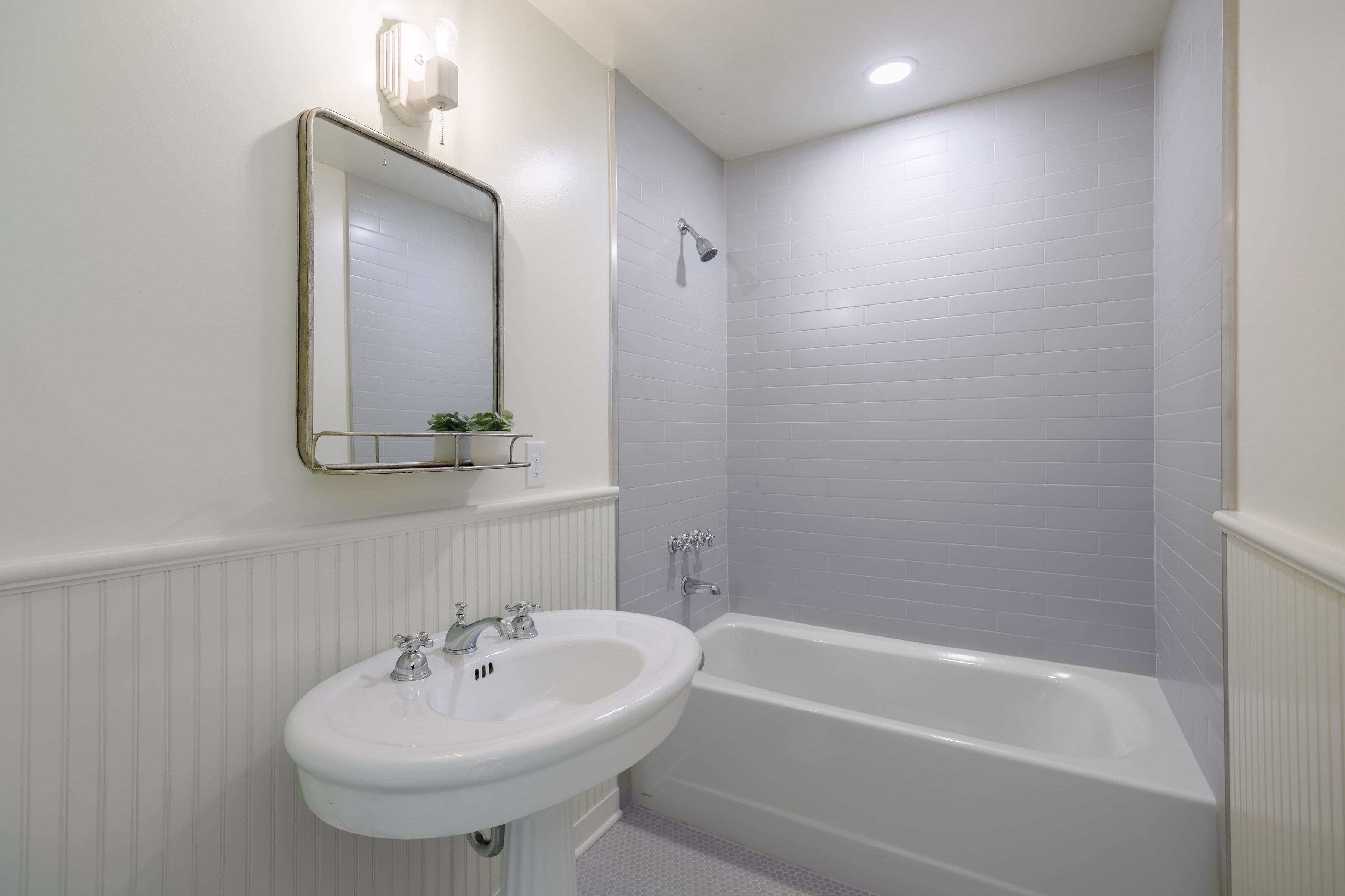 A modern bathroom featuring a white sink, tub, and a wall mirror.