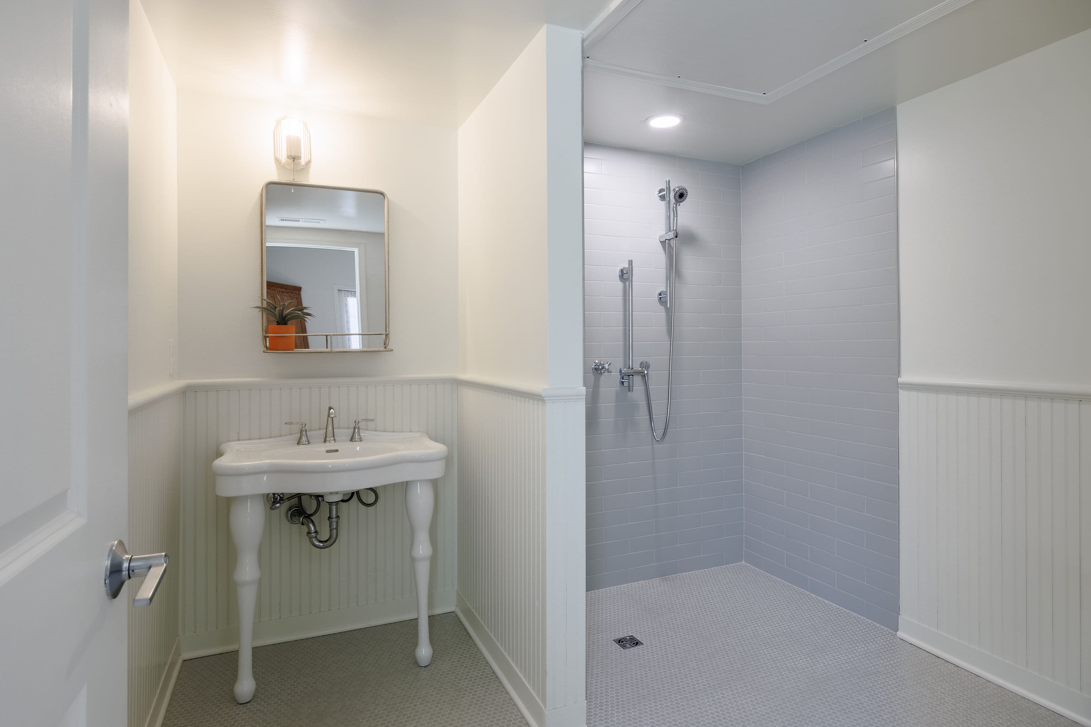 A modern bathroom featuring a white pedestal sink and a separate shower area with light gray tiles.