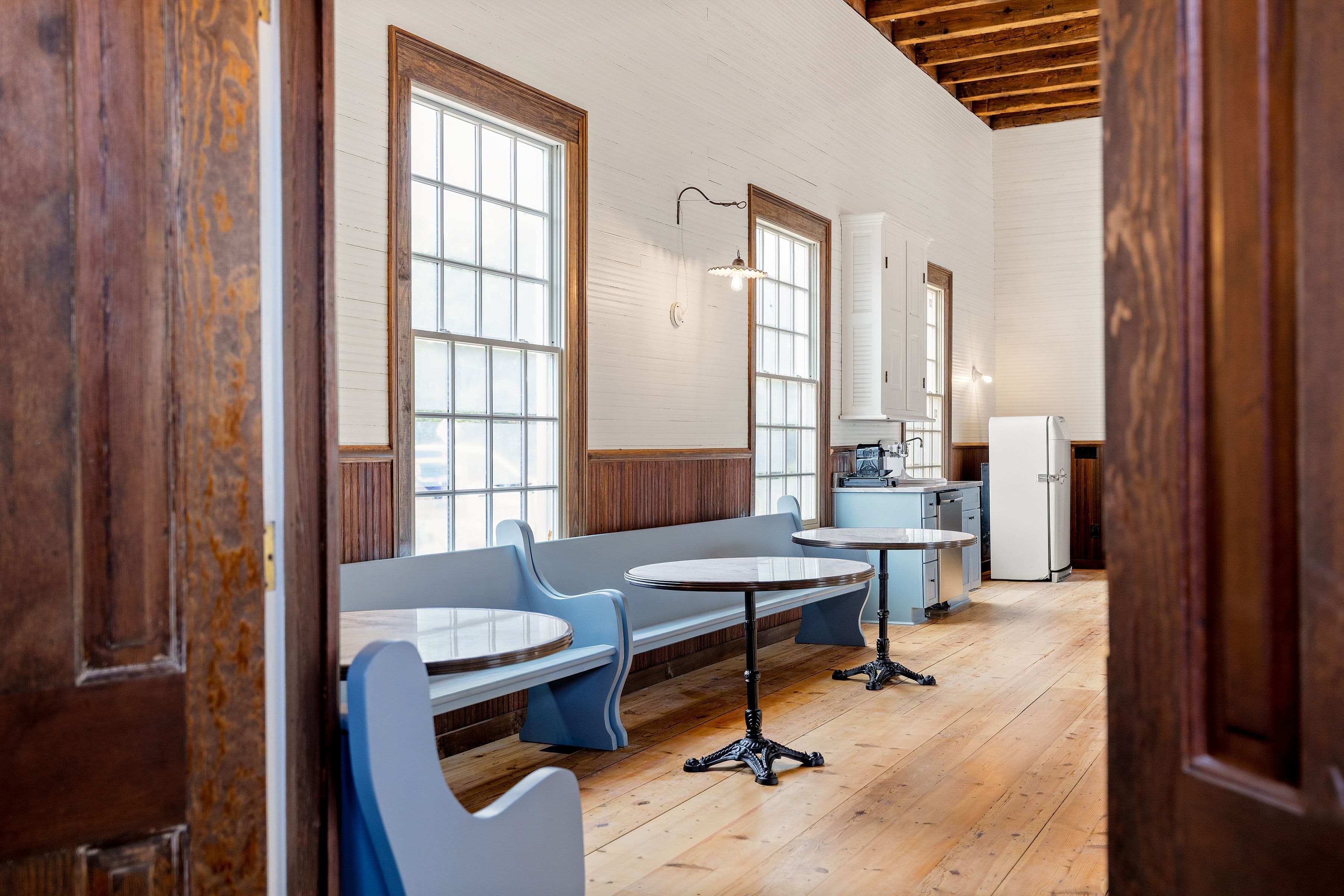 A bright, rustic interior featuring blue seating and a kitchen area with vintage appliances.